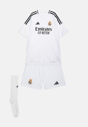 Conjunto de camiseta y pantalones cortos del Real Madrid en blanco, con detalles en negro y las franjas de Adidas. Incluye un calcetín blanco. Logotipo del equipo mostrado.