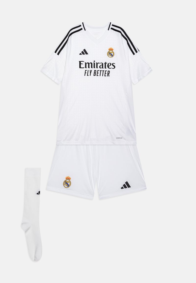 Completo da calcio del Real Madrid composto da maglia e pantaloni in bianco, con dettagli neri e strisce Adidas. Include una calza bianca. Logo della squadra in evidenza.