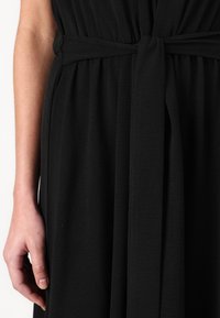 Black dress made of soft fabric, featuring a tied belt at the waist and subtle texture, with fabric draping down from the waist.