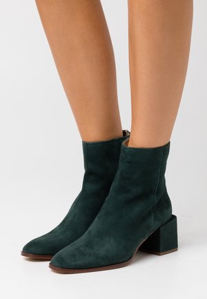 Botas de tobillo de ante verde con punta afilada y tacón cuadrado. Textura suave, diseño sencillo y detalle de cremallera disponible en la parte posterior.