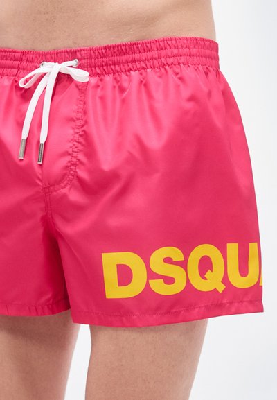 Κόκκινα μαγιό με ελαστική μέση, λευκό κορδόνι και μεγάλο κίτρινο κείμενο "DSQUARED" στο αριστερό πόδι. Λείο, λαμπερό ύφασμα.