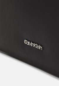 Schwarzes strukturiertes Lederaccessoire mit silberner, geprägter "Calvin Klein"-Logodetail. Glatte Oberfläche mit dezentem Kornmuster.