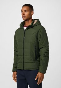 Chaqueta aislante verde con cierre frontal de cremallera, capucha ajustable y bolsillo lateral con cremallera. Presenta un diseño acolchado y un interior en contraste.