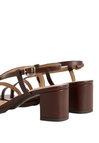 Le sandali in pelle marrone presentano sottili cinturini e un tacco quadrato. Il dettaglio con fibbia regolabile completa il design.