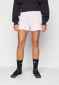 Svetlo roza športne hlače s elastičnim pasom in stranskimi žepi, v kombinaciji z črnimi nogavicami in supergami z belimi akcenti.