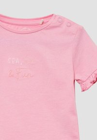 Roze T-shirt met korte mouwen van zachte katoen met gerimpelde mouwkanten. Voorzien van geborduurde tekst "ZEE, ZON & Plezier" in contrasterende pastelkleuren.
