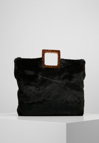 Svart väsk av konstpäls med ett fyrkantigt handtag i bärnstensfärgad resin. Väskan har en mjuk textur och en rymlig, rektangulär form.