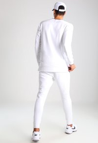 White sweatshirt and sweatpants set, cotton material, relaxed fit, straight-leg pants, ribbed cuffs, and a smooth texture. Worn with a white cap.