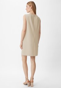 Knielanges, ärmelloses Kleid aus leicht beigem Stoff mit strukturierter Oberfläche, ausgestattet mit einem dezenten Reißverschluss auf der Rückseite und einem geraden Schnitt.