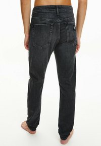 Jeans de mezclilla negra con corte recto, que cuentan con dos bolsillos traseros y un pespunte sutil. La cinturilla es lisa, sin adornos.
