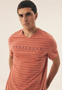 Czerwono-biała w paski koszulka z krótkim rękawem w serek, wykonana z miękkiego materiału, z wyraźnym napisem "HENDERSON YACHT CLUB".
