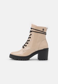 Bottines en cuir verni beige avec lacets noirs, talon noir épais et languette à tirer, dotées d'une semelle en caoutchouc texturée et d'une finition lisse.