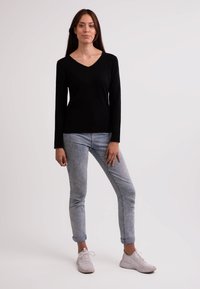 Sort V-hals sweater, lange ærmer, tætsiddende design. Lyseblå jeans, tapered ankelsnit. Hvide sneakers, tekstureret overflade. Enkel, moderne stil.