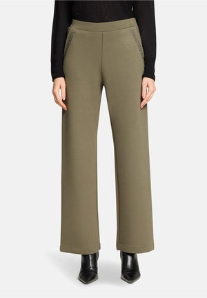 Pantalon vert olive à jambes larges en tissu doux, doté de poches latérales avec des détails subtils, associé à des bottes noires à talons.