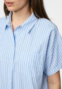 Niebieska i biała w paski koszula z krótkim rękawem, z wyrazistym kołnierzykiem i kieszenią na piersi, wykonana z lekkiego materiału o gładkiej teksturze.