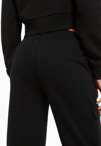 Pantaloni jogger neri in cotone con vita elastica e dettagli con tasche laterali. Il tessuto è morbido e liscio, con un design a gamba affusolata.