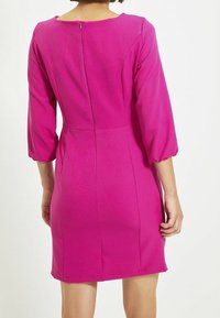 Vestido ajustado, hasta la rodilla, en un rosa brillante con cuello redondo, mangas 3/4 y cremallera trasera oculta; textura suave con costuras mínimas.