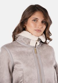 Giacca in pelle sintetica grigia con un morbido colletto in shearling crema, chiusura anteriore con zip e tasche con zip, caratterizzata da superfici lisce e testurizzate.