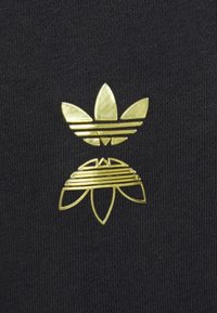 Zlatý dizajn loga so vrstvenými tvarmi listov a kvetov na čiernom textúrovanom pozadí.