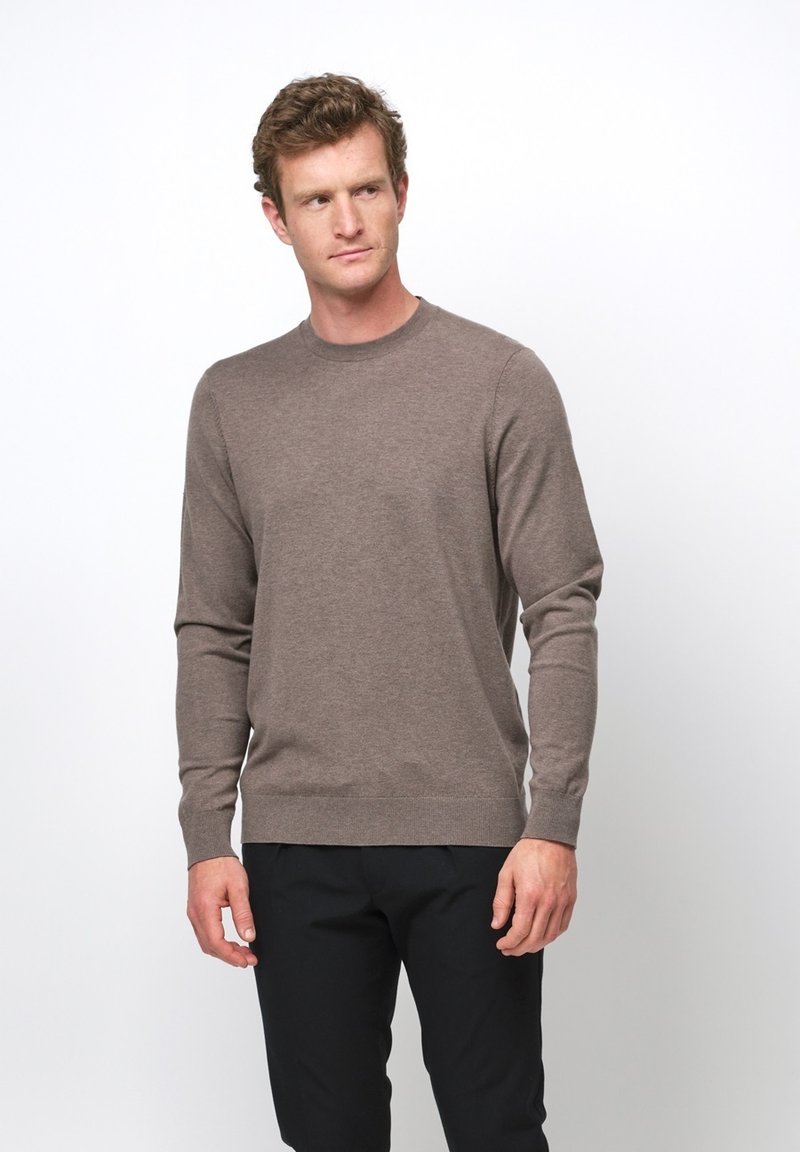Maglione marrone a maniche lunghe con collo a girocollo realizzato in tessuto morbido. Presenta un collo e polsini a coste, indossato sopra pantaloni scuri.