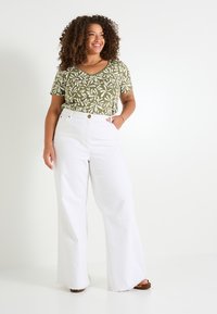 Camiseta de pico verde con patrón floral combinada con pantalones vaqueros de pierna ancha blancos de talle alto. Los jeans tienen un dobladillo deshilachado y cierre frontal con botones.