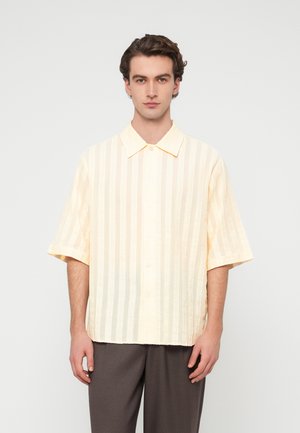 Κοντομάνικο πουκάμισο σε απαλό κίτρινο με κάθετες ρίγες. Κατασκευασμένο από ελαφρύ ύφασμα, με κουμπιά μπροστά και κλασικό γιακά.