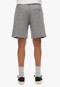 Pantalones cortos de algodón gris con un acabado texturizado, que cuentan con un bolsillo trasero y una cintura elástica, combinados con calcetas y zapatillas negras.
