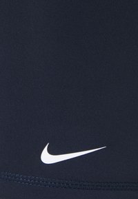 Navy urheilusortsit, valmistettu joustavasta kankaasta, joissa on valkoinen Nike-logo alhaalla oikealla ja tasosauma alareunassa.