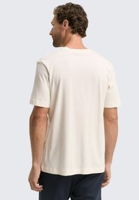 Korte mouwen, crème t-shirt van zachte katoen. Heeft een ontspannen pasvorm, ronde halslijn en omzomen mouwen.