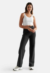 Cropped top sportivo bianco e pantaloni neri a vita alta con una texture liscia. Il modello si trova in una posizione rilassata su uno sfondo neutro.