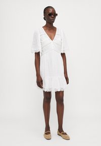 Hvit kort kjole med korte ermer, prikket tekstur, blondekant i helen og V-hals. Brukt med lysebrune flats og solbriller.