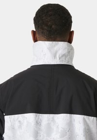 Chaqueta en blanco y negro con cuello blanco texturizado, que presenta un diseño a bloques de color y un acabado suave. Sin cierres o adornos visibles.