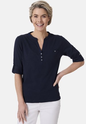 Marineblaue Hemd mit Henley-Ausschnitt, drei Knöpfen, hochgekrempelten Ärmeln und einer kleinen Brusttasche. Weicher Stoff und lockere Passform.