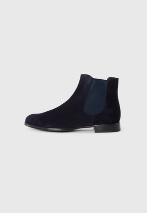 Bottines Chelsea en daim bleu marine avec semelle noire et panneau élastique sur le côté, présentées en profil gauche sur un fond clair et uni.