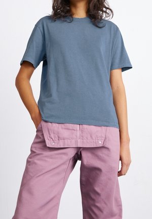 Bawełniany t-shirt w kolorze łupkowo-niebieskim, z krótkimi rękawami i okrągłym dekoltem; zestawiony z jasnoróżowymi spodniami z kieszenią i zatrzaskami.