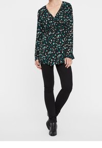 Blusa nera a maniche lunghe con scollo a V profondo, caratterizzata da un motivo di foglie multicolori in tonalità di verde acqua e crema, abbinata a jeans skinny neri.