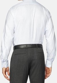 Långärmad ljusblå randig skjorta i kombination med mörkgrå byxor. Skjortan har en knapp-down krage och manschettaccenter. Svart läderbälte synligt.