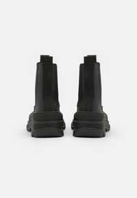 Botas de tornozelo pretas com um cabedal liso, painéis laterais elásticos e uma sola espessa e texturizada com um padrão robusto para tração.