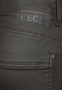 Mörkgrå denimbyxor med en texturerad yta. Funktioner inkluderar en svart logotagga, dekorativ sömnad och metallfästen på fickorna.