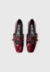 Un paio di eleganti ballerine bordeaux a punta quadrata con tre cinturini borchiati e soletti neri brandizzati "REPLAY" su sfondo bianco.