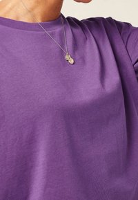 Fioletowa koszulka bawełniana z okrągłym dekoltem, charakteryzująca się gładką fakturą i krótkimi rękawami. W zestawie znajduje się naszyjnik z srebrnym wisiorkiem jako dodatek.