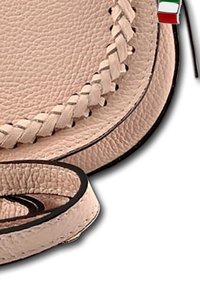 Beige leren handtas met een gevlochten ontwerpdetaillering langs de rand, met een ronde vorm en zwarte accenten. Inclusief een klein driekleurig label.