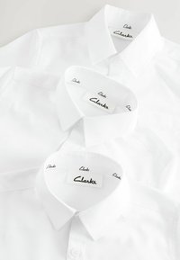 Tri bijele košulje s dugmadi na ovratniku, s oznakama "Clarks" unutar izreza, od glatkog materijala.