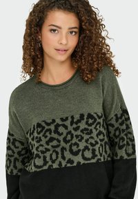 Sweter wykonany na drutach w oliwkowym kolorze z czarnym wzorem w panterę na wysokości klatki piersiowej oraz jednolitą czarną dolną częścią. Okrągły dekolt i teksturowana tkanina.