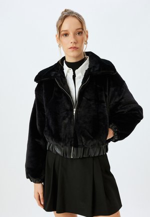 Sort faux fur jakke med en cropped design, lynlås lukning og elastisk kant. Har en bred krave og ribbede manchetter.