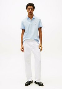 Polo shirt in cotone azzurro chiaro con dettagli gialli, abbinato a pantaloni bianchi e scarpe nere. Design semplice, maniche corte e colletto classico.