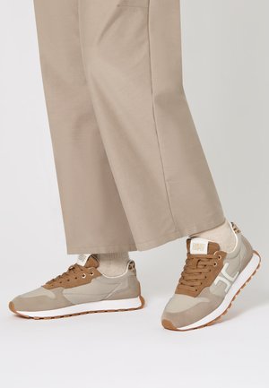 Sneaker beige e marroni realizzati in materiali di pelle e suede, dotati di un logo bianco, lacci marroni e una suola in gomma testurizzata.