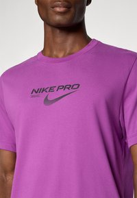 Lilla Nike Pro t-shirt lavet af blødt stof, med et sort logo og tekst på forsiden, med en klassisk rund halsudskæring og korte ærmer.