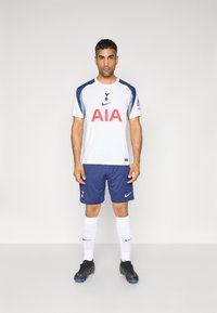 Hvid atletisk trøje med marineblå accenter, prydet med "AIA" i rødt, parret med marineblå shorts og hvide sokker, sorte fodboldstøvler, Spurs-logo.