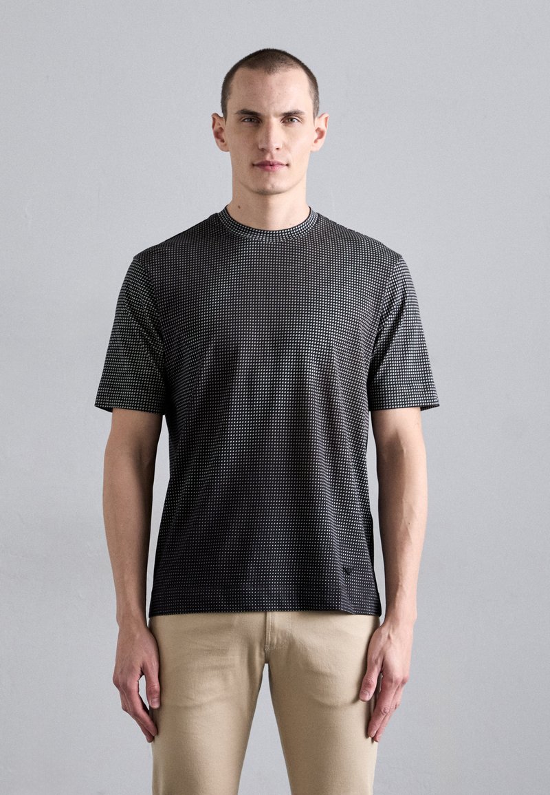 Short-sleeve, black T-shirt with a dotted pattern, round neckline, and slim fit, paired with light beige pants. Smooth texture and minimal detail.